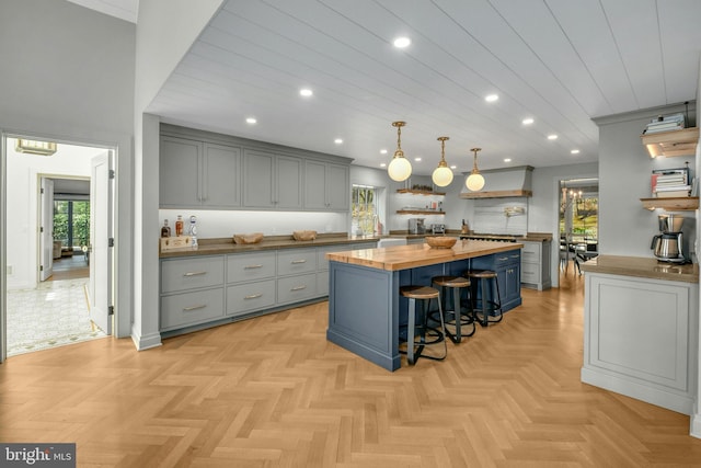 kitchen with a center island, decorative light fixtures, wood counters, light parquet flooring, and a breakfast bar area