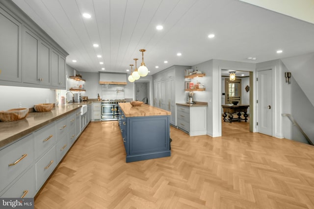 kitchen with wood counters, wall chimney exhaust hood, a kitchen island, light parquet floors, and hanging light fixtures