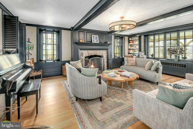 living room with beamed ceiling, light hardwood / wood-style floors, and a stone fireplace