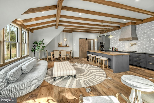 living room with lofted ceiling with beams, a barn door, and wood-type flooring