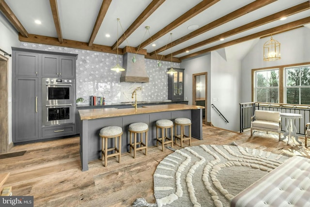 kitchen with premium range hood, stainless steel double oven, gray cabinetry, a breakfast bar area, and hanging light fixtures