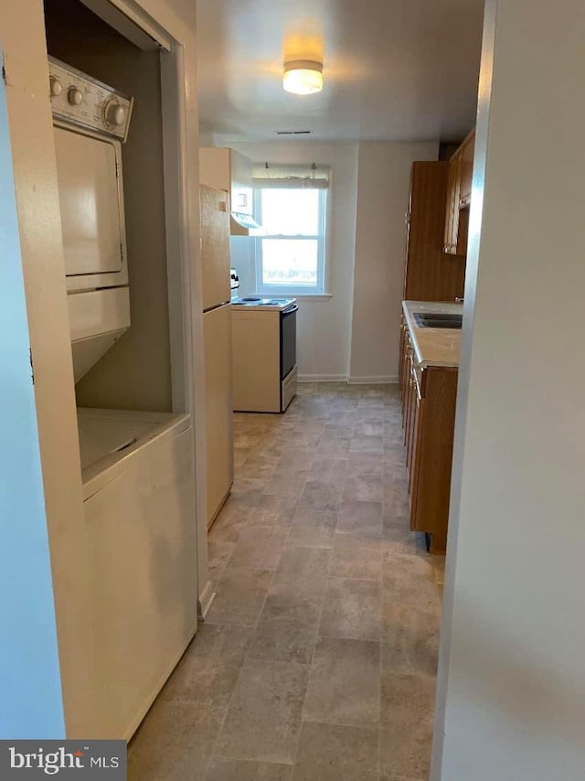 kitchen with light tile floors, white refrigerator, stacked washer / drying machine, range with electric stovetop, and sink