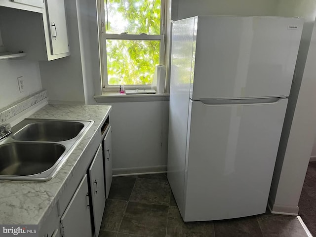 kitchen with dark tile floors, white cabinetry, sink, and white refrigerator