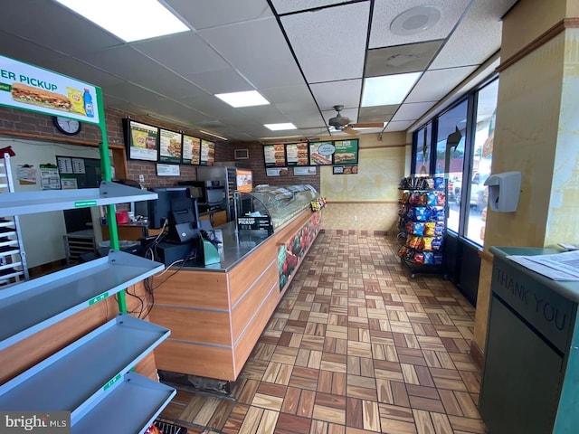 interior space with a paneled ceiling, brick wall, ceiling fan, and light tile floors