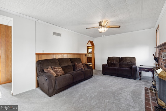 carpeted living room featuring a brick fireplace, ceiling fan, and crown molding