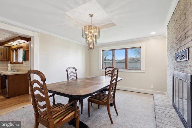 dining space featuring sink, crown molding, a fireplace, a notable chandelier, and light wood-type flooring