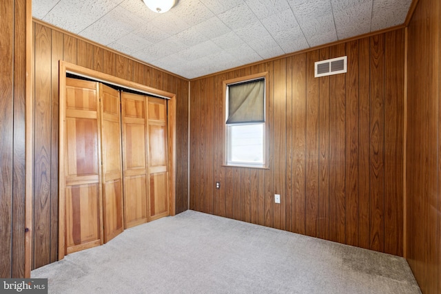 unfurnished bedroom with carpet flooring, a closet, and wood walls