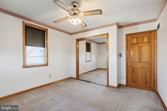 unfurnished bedroom with light carpet, a closet, ceiling fan, a textured ceiling, and ornamental molding