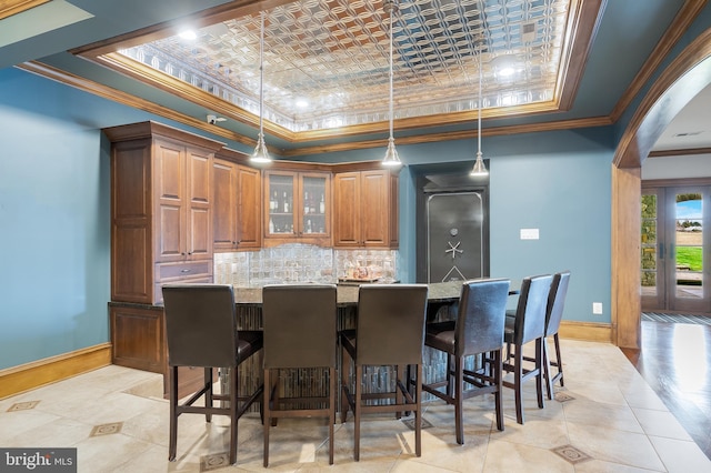 kitchen with a raised ceiling, light stone countertops, crown molding, and hanging light fixtures