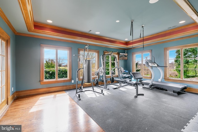 workout room featuring a raised ceiling, ornamental molding, and light wood-type flooring