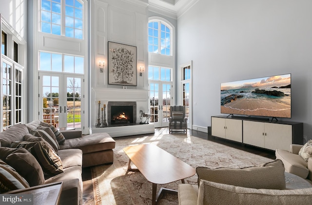 living room with a large fireplace, crown molding, french doors, and a towering ceiling