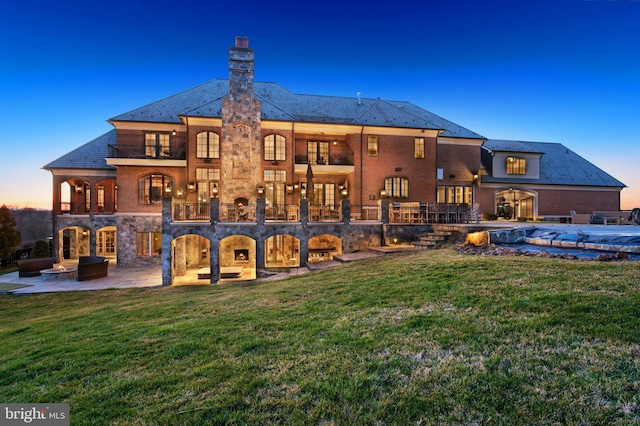 back house at dusk with a patio area, a balcony, a yard, and a covered pool