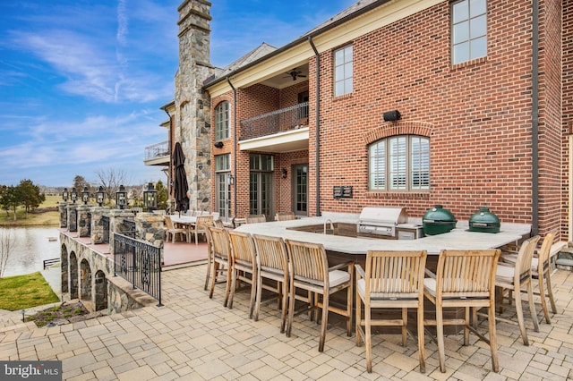 view of patio with a water view, grilling area, a balcony, and ceiling fan