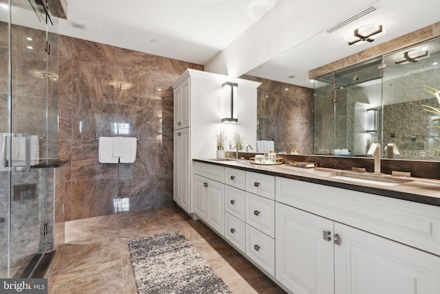 bathroom with tile floors, a shower with shower door, tile walls, oversized vanity, and dual sinks