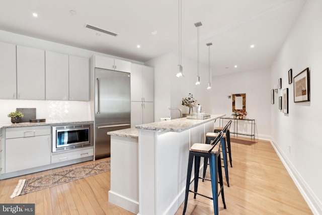 kitchen featuring built in appliances, decorative light fixtures, light wood-type flooring, a kitchen island, and white cabinets