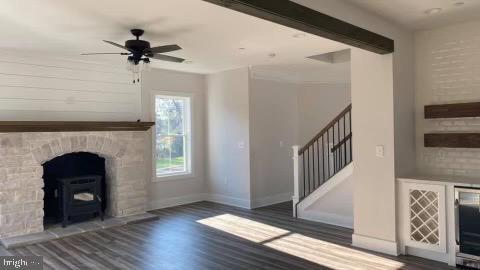 unfurnished living room featuring beam ceiling, dark hardwood / wood-style floors, a wood stove, and ceiling fan