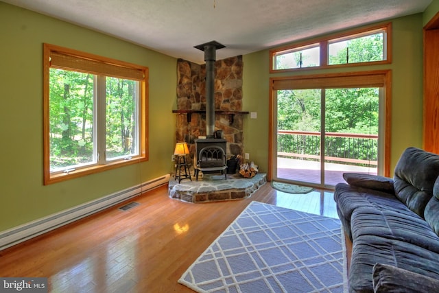 living room with a wood stove, hardwood / wood-style floors, baseboard heating, and a healthy amount of sunlight