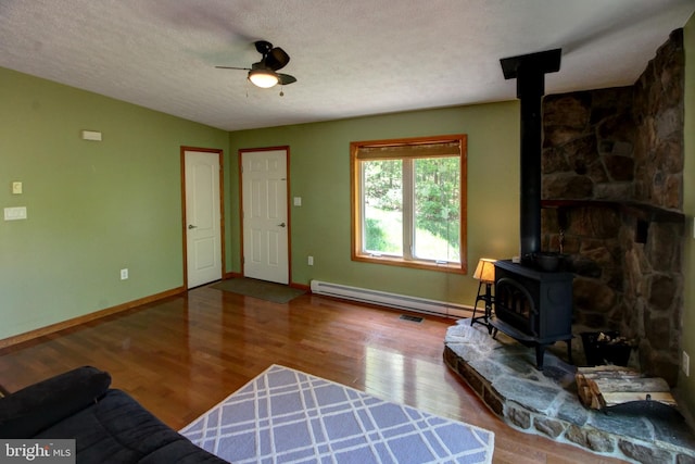 living room with a wood stove, hardwood / wood-style flooring, ceiling fan, and a textured ceiling