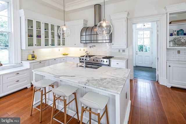 kitchen with white cabinets, a breakfast bar area, wall chimney exhaust hood, and a healthy amount of sunlight