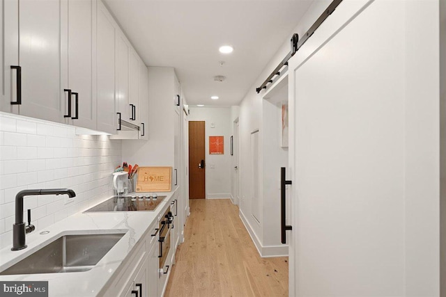 kitchen with light stone counters, light hardwood / wood-style floors, a barn door, white cabinets, and sink