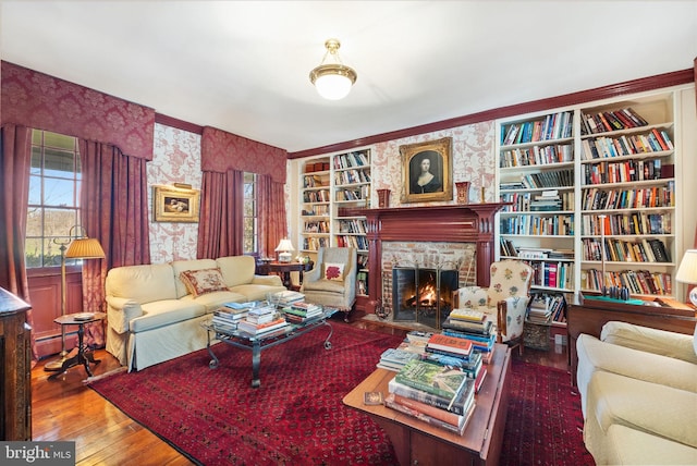 living room with built in shelves, hardwood / wood-style flooring, and a brick fireplace