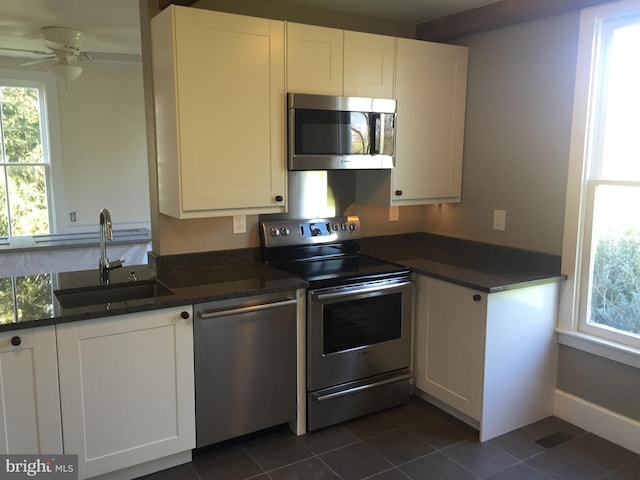 kitchen with stainless steel appliances, ceiling fan, dark tile patterned floors, sink, and white cabinetry