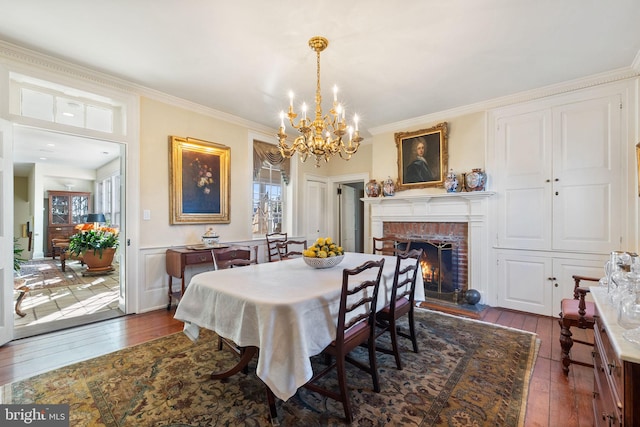 dining space featuring a fireplace, dark hardwood / wood-style flooring, an inviting chandelier, and crown molding