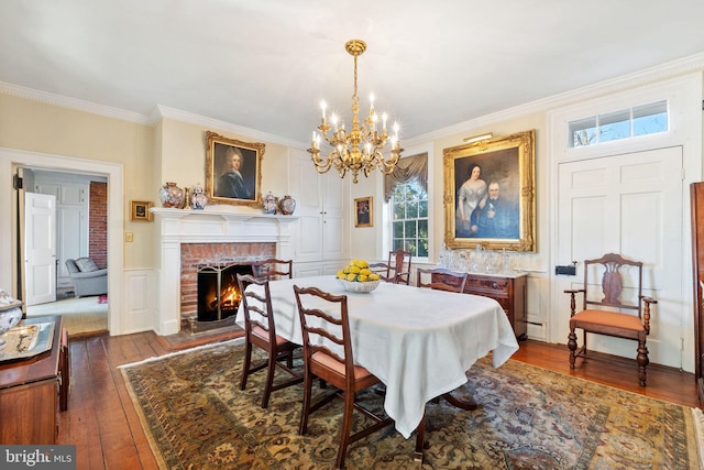 dining area with a notable chandelier, a fireplace, ornamental molding, and dark wood-type flooring