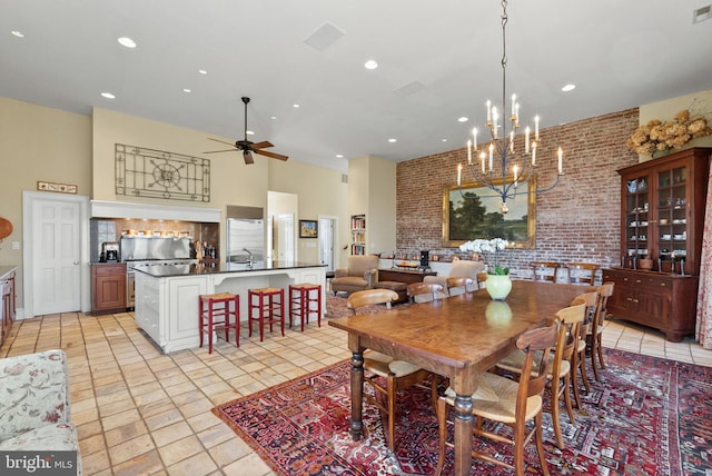 dining area with ceiling fan with notable chandelier, a towering ceiling, sink, and brick wall