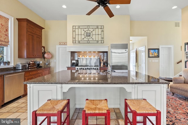 kitchen with a kitchen bar, stainless steel appliances, dark stone countertops, and an island with sink