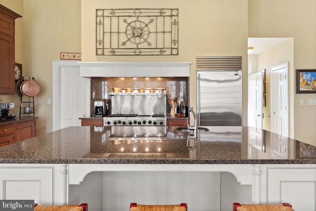 interior space featuring sink, dark stone countertops, stove, a kitchen bar, and stainless steel built in fridge