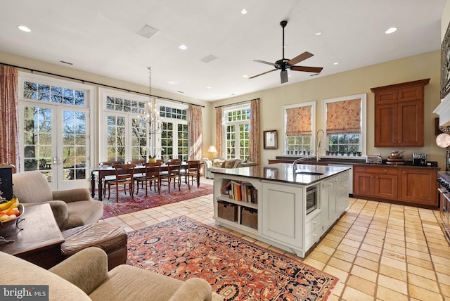 kitchen featuring stainless steel microwave, decorative light fixtures, a kitchen island with sink, white cabinets, and ceiling fan with notable chandelier