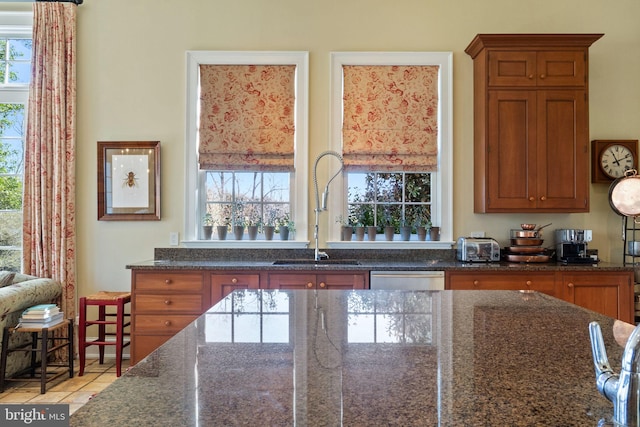 kitchen with dark stone countertops, sink, light tile patterned floors, and stainless steel dishwasher