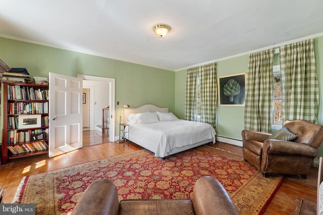 bedroom with hardwood / wood-style floors, a baseboard radiator, and crown molding