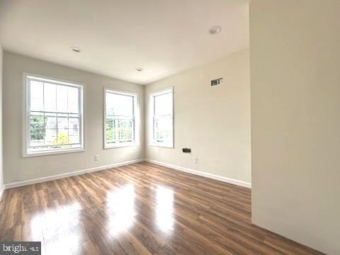 unfurnished room featuring plenty of natural light, wood finished floors, and baseboards