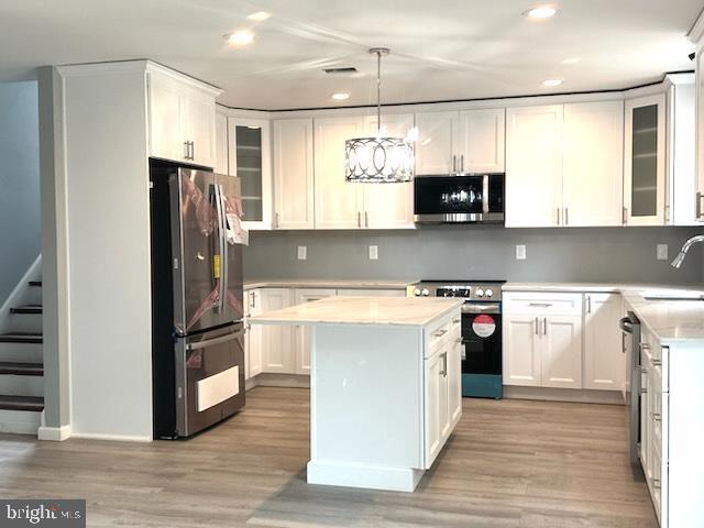 kitchen featuring a kitchen island, appliances with stainless steel finishes, light wood-type flooring, white cabinetry, and a sink