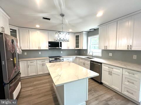 kitchen featuring visible vents, white cabinets, appliances with stainless steel finishes, light wood-type flooring, and a sink