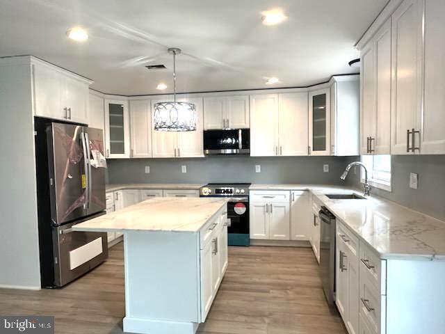 kitchen featuring stainless steel appliances, a kitchen island, a sink, and white cabinetry