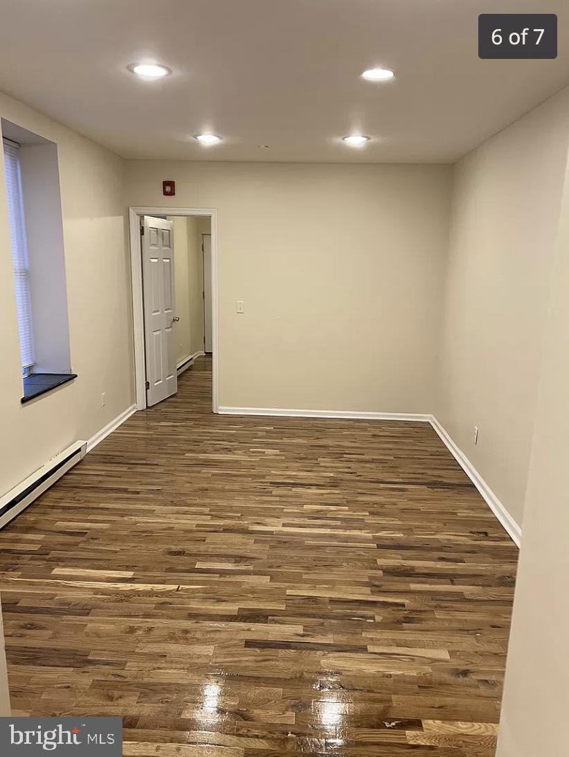 unfurnished room with dark hardwood / wood-style floors and a baseboard heating unit