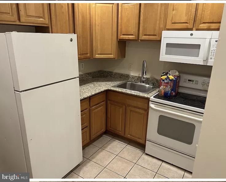 kitchen featuring white appliances, stone counters, sink, and light tile floors