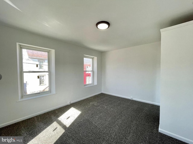 spare room with dark colored carpet and a wealth of natural light