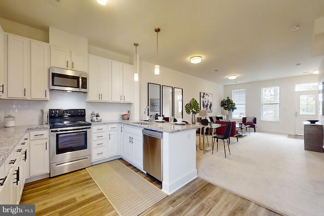 kitchen with hanging light fixtures, white cabinetry, appliances with stainless steel finishes, sink, and light hardwood / wood-style flooring