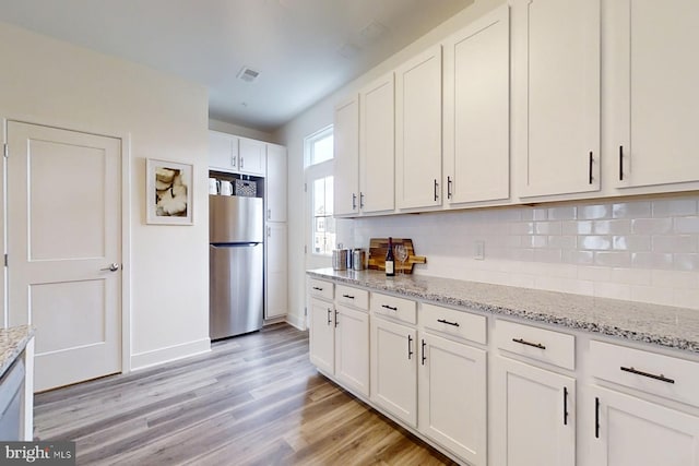 kitchen with light stone countertops, backsplash, light hardwood / wood-style flooring, white cabinets, and stainless steel refrigerator