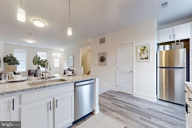 kitchen featuring pendant lighting, stainless steel appliances, light stone countertops, white cabinetry, and light wood-type flooring