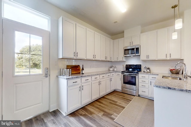 kitchen featuring light hardwood / wood-style flooring, appliances with stainless steel finishes, white cabinets, hanging light fixtures, and sink