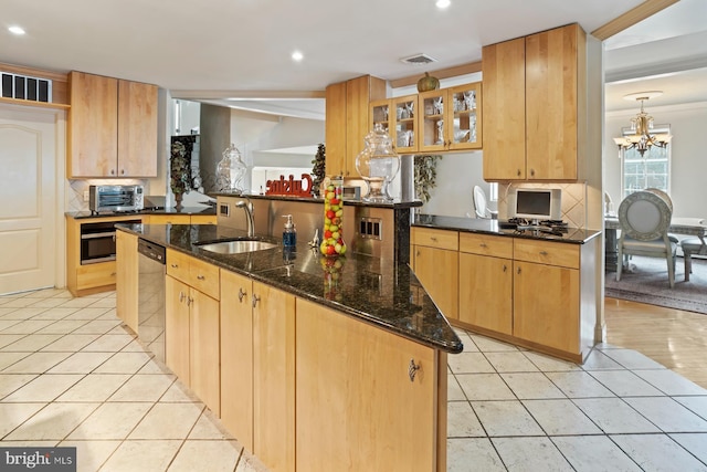 kitchen featuring a notable chandelier, sink, an island with sink, dark stone countertops, and tasteful backsplash