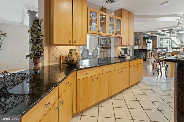 kitchen with backsplash, dark stone countertops, light tile floors, crown molding, and ornate columns