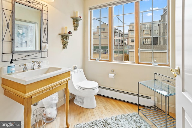 bathroom with toilet, plenty of natural light, large vanity, a baseboard heating unit, and wood-type flooring