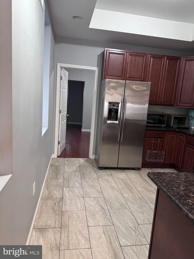 kitchen with light tile flooring, a skylight, dark stone counters, and stainless steel refrigerator with ice dispenser