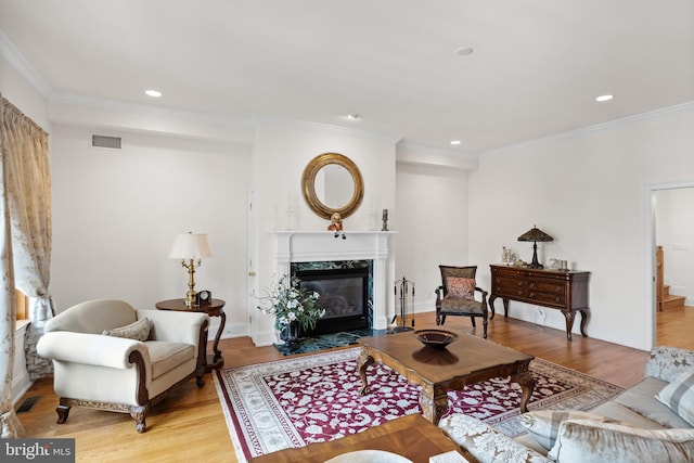 living room with a high end fireplace, light hardwood / wood-style floors, and ornamental molding